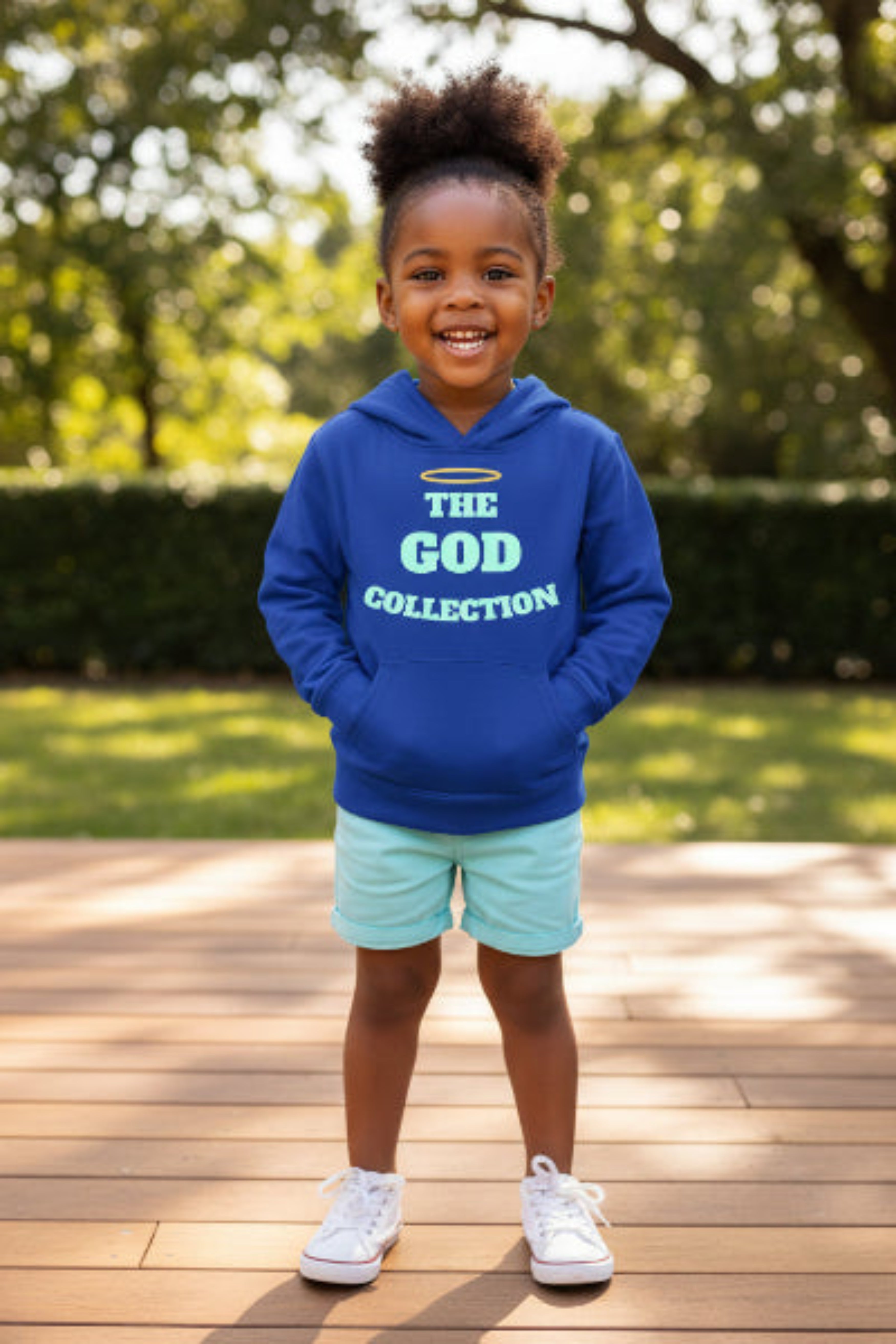 Child wearing a blue hoodie with 'The God Collection' text, standing on a wooden deck with greenery in the background.