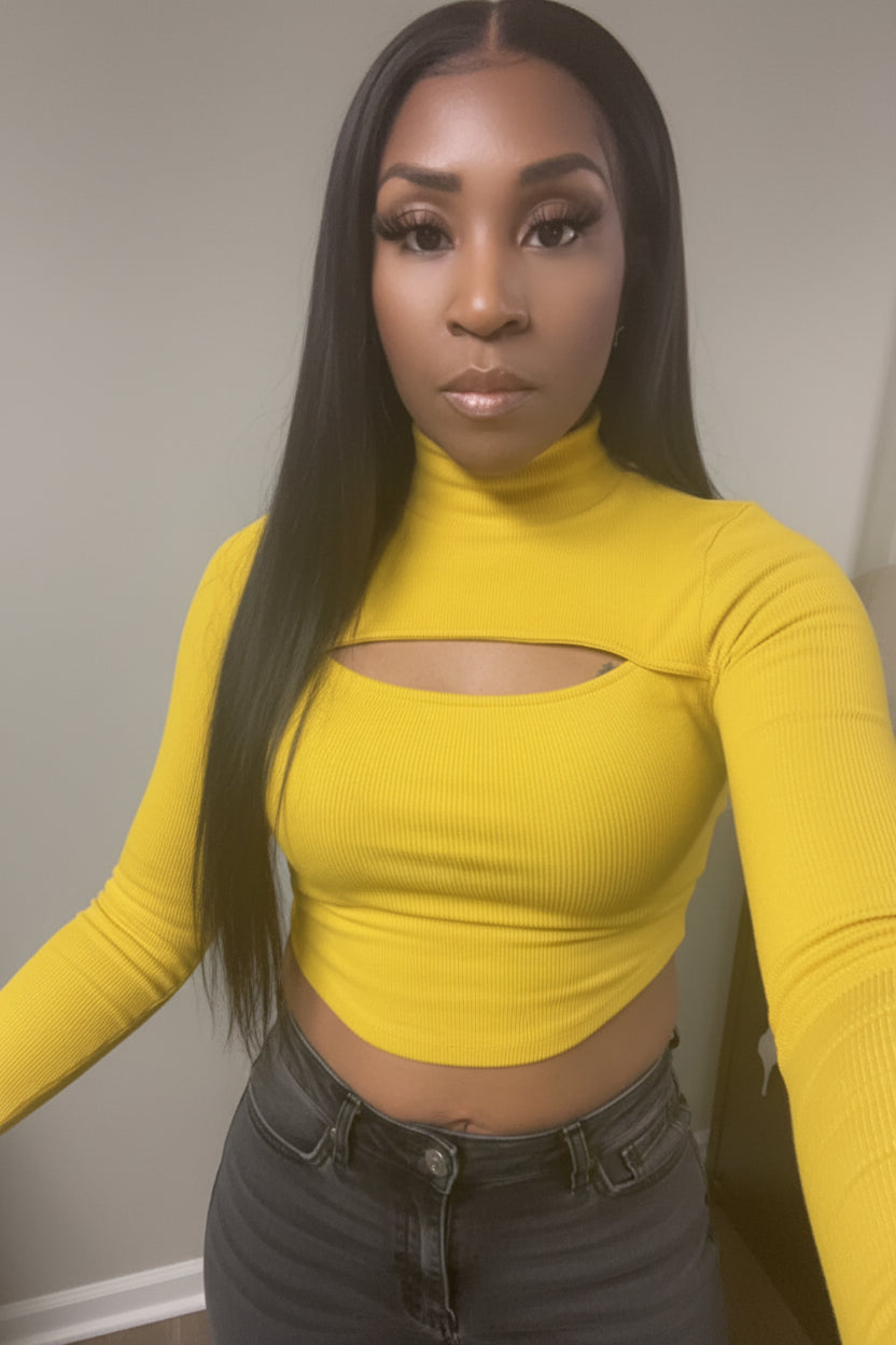 A person wearing a yellow cropped cut-out long-sleeve mock neck sweater with a red hat.